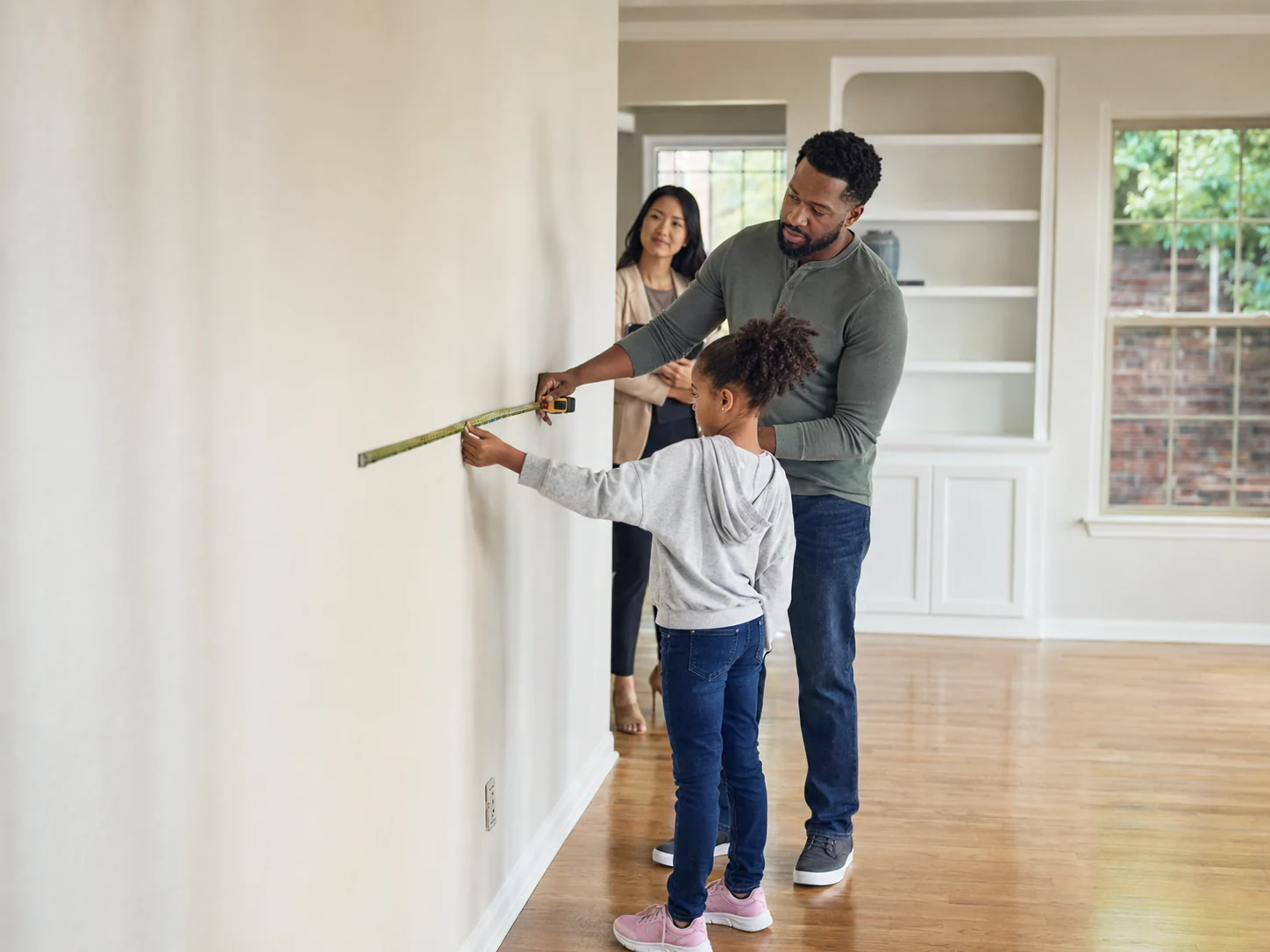 A family measuring a wall in the empty living room of their first home